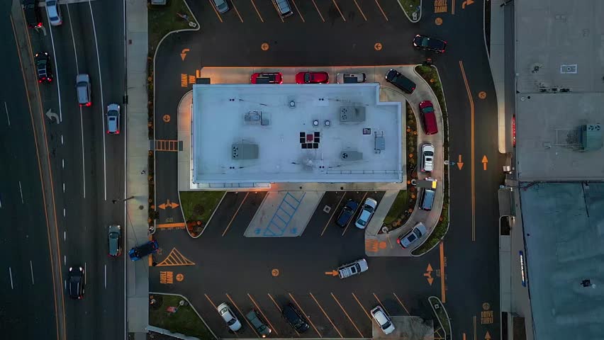 A top down, aerial view directly over a busy fast food restaurant with a drive through for orders on the go. The camera is stationary as it hovers, tilted straight down above the restaurant roof. Royalty-Free Stock Footage #3395397421