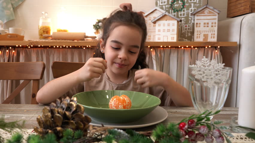 A girl sits at a festive table and eats enjoys delicious tangerine. New Year Eve