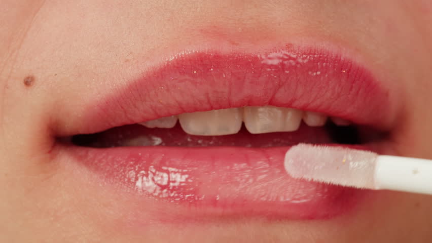 Beauty lip care. Young woman applying hygienic lipstick on lips close-up on pink background. Make-up routine