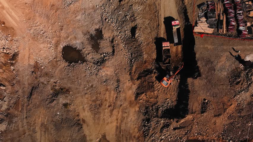 Excavator is loading ground with rubble into a truck on construction site filmed from above by drone at day time somewhere in Georgia. Building roads and necessary communications in Tbilisi theme