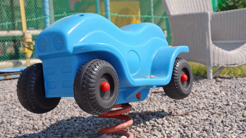 Close-up of empty children plastic toy car on spring on playground in yard attraction is swinging by inertia, child has disappeared kidnapping Fenced area for children's games, family amusement park