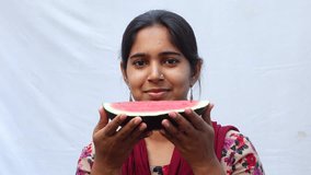 An Asian girl eating a slice of red watermelon on a white background. Young girl eating fresh watermelon fruit. Diet control concept 4k video.