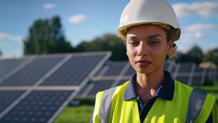 Close up portrait of female engineer wearing hard hat and hi vis safety vest outdoors inspecting solar panels on sustainable energy farm - shot in slow motion Royalty-Free Stock Footage #3395627431
