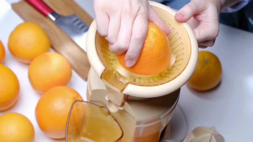 Close up of hands squeezing orange for juice. Human using their hands to squeeze half orange to make the orange juice into the glass. Making orange juice pressing half of lemon. Royalty-Free Stock Footage #3395786133