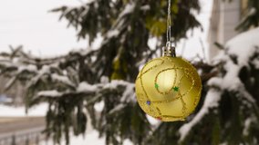One yellow Christmas ball weighs near snow-covered branches on a semi-blurred background