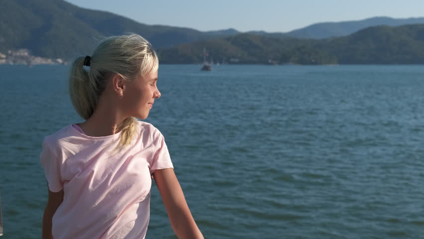 Teen look around blue sea. A cute modern teen girl enjoy the wind on her face on lake pier in summer.