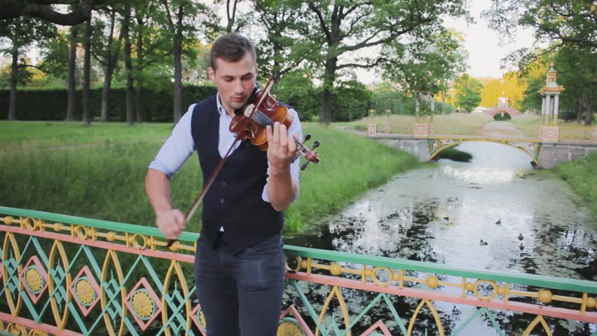 Man playing the violin . young musician artist violinist enthusiastically with violin in hands in vest and shirt ,playing the violin in the park .concept hobby music public performance practice
