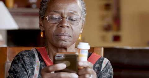 Happy smiling black woman over 50 refilling her medication prescription drugs online using smart phone technology app in her home