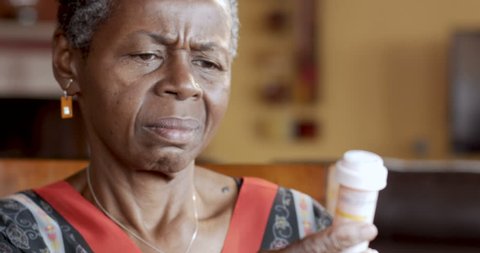 Black senior woman putting on glasses to read medication instructions of her prescription bottle for her health care