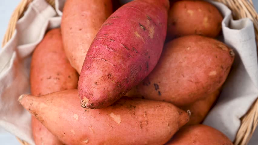 Whole raw sweet potatoes in a basket, on bright background, top view.