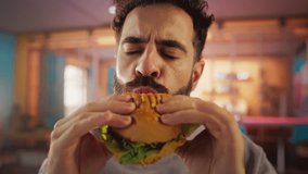 Tracking Slow Motion Portrait of a Man Who is Enjoying a Delicious Hamburger at Home. Colorful Setting For a Happy Male Who Ordered Fast Food Delivery, Approving of the High Quality - Powered by Shutterstock - Get 15% off with code: PIKWIZARD15