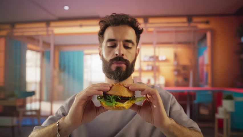 Tracking Slow Motion Portrait of a Man Who is Enjoying a Delicious Hamburger at Home. Colorful Setting For a Happy Male Who Ordered Fast Food Delivery, Approving of the High Quality Royalty-Free Stock Footage #3395921123