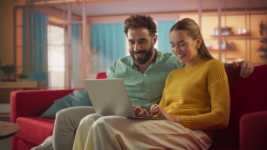 Portrait of Young Couple Using Laptop Computer While Sitting on a Couch at Home. Engaged Couple Doing Online Shopping for their Wedding Preparations, Discussing Different Options Using Technology - Powered by Shutterstock - Get 15% off with code: PIKWIZARD15