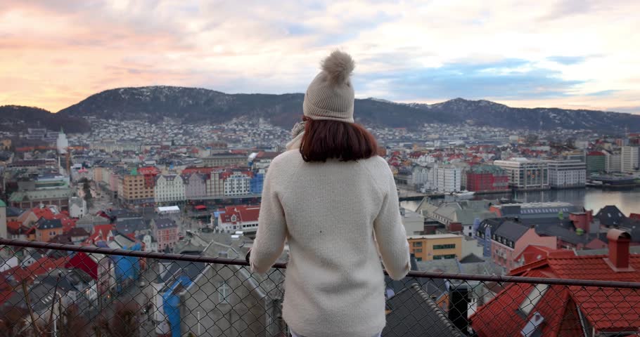 A tourist woman enjoys the panoramic winter sunrise view of the cityscape of Bergen, Norway