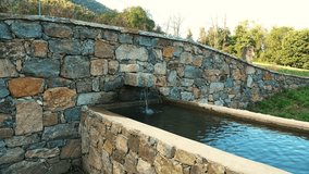 A mountain spring. Drinking water for animals. A stone waterfall. A trough filled with water from the mountain spring. A metal fountain with potable water.