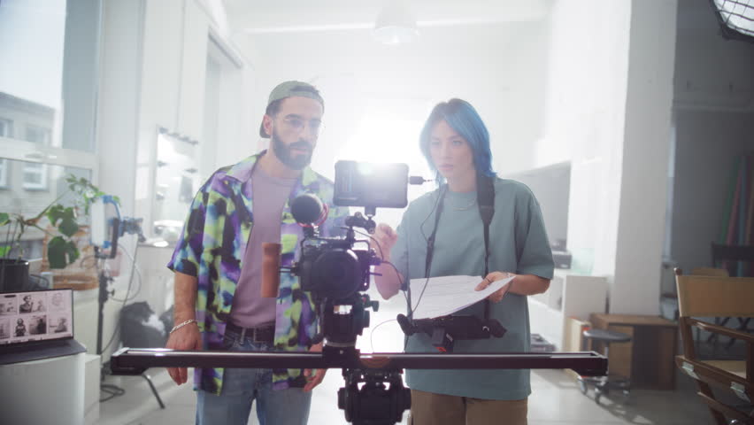 Young Female Director Giving Instructions to Male Cinematographer about Filming a Video in a Bright Studio. Professional Crew Members Working Together as a Team to Capture Aesthetic Footage on Camera Royalty-Free Stock Footage #3396005741