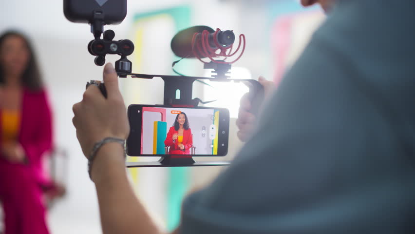 Young Female Content Creator Working with her Cinematographer to Film a Video in Bright Minimalistic Set. New Generation of Filmmakers Using Smartphone to Shoot Budget-Friendly, High-Quality Project