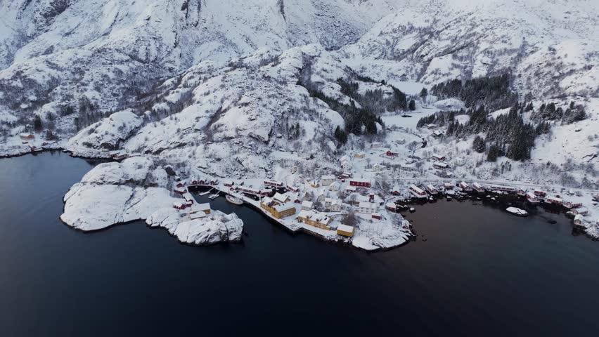 Winter wonder in motion: A drone glides forward, revealing the Nusfjord Fishing Village, Fjord, and Mountains in the Lofoten Islands, Norway, with a captivating downward tilt.