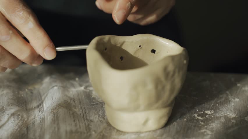 A woman makes holes using a tool in a clay craft - a candlestick. Close-up. Hobbies and creativity.