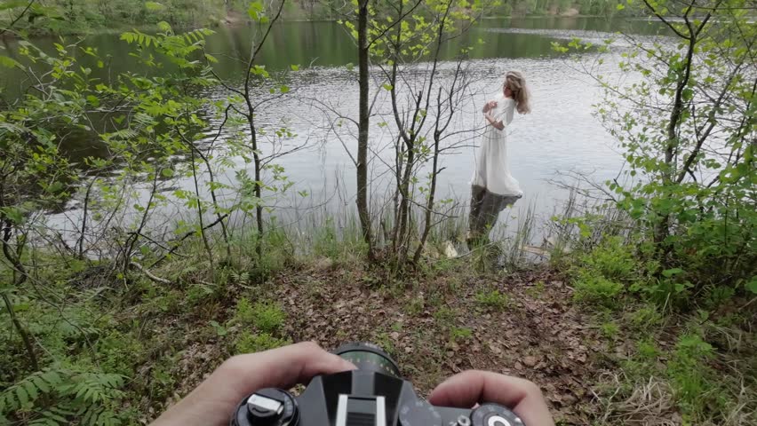 Photographer with analog 35mm film camera taking pictures of young beautiful woman model in white dress at nature. Woman in a lake.