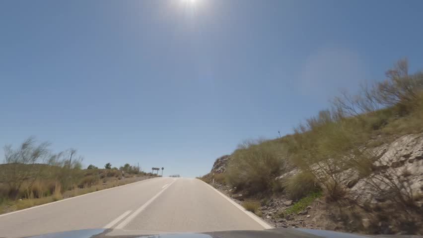 First person view, FPV, from dashcam of car driving mountain road from Calar Alto Observatory to Tabernas Desert in Almeria, Andalusia, Spain, Europe. Road trip in POV, with bright, sunny, clear sky	
