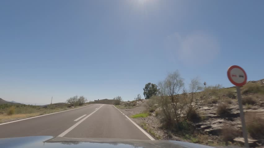 First person view, FPV, from dashcam of car driving mountain road from Calar Alto Observatory to Tabernas Desert in Almeria, Andalusia, Spain, Europe. Road trip in POV, with bright, sunny, clear sky	