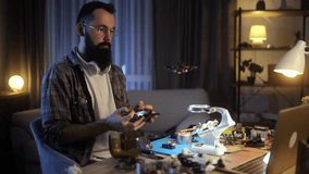 Creating and piloting drones. A young, bearded man in a plaid shirt tests his FPV drone after it has been assembled. Hobbies