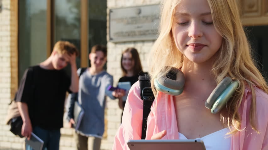 Self-assured young lady at ease being solitary in university. Young woman takes deep breath of air smiling against classmates