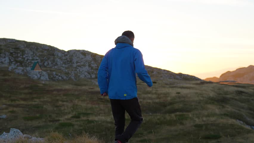 A hiker going towards wooden mountain shelter house at sunrise behind rocky ridge