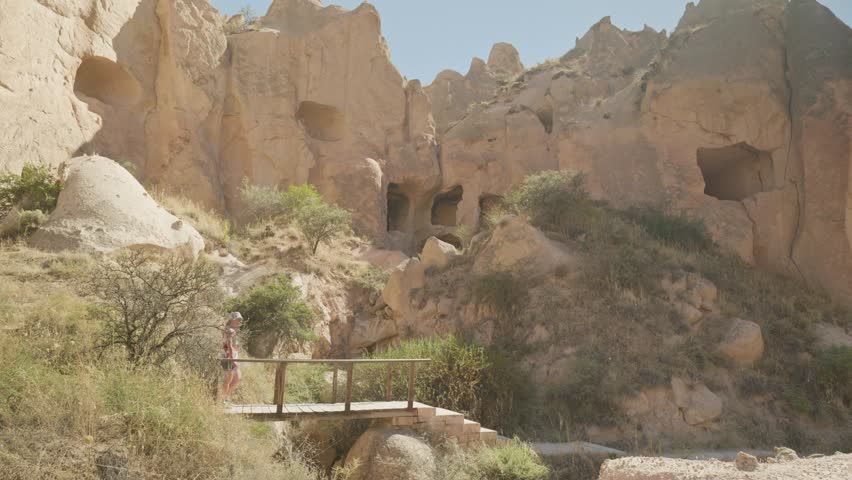 Female explorer tourists walks over wooden bridge in dramatic landscape
