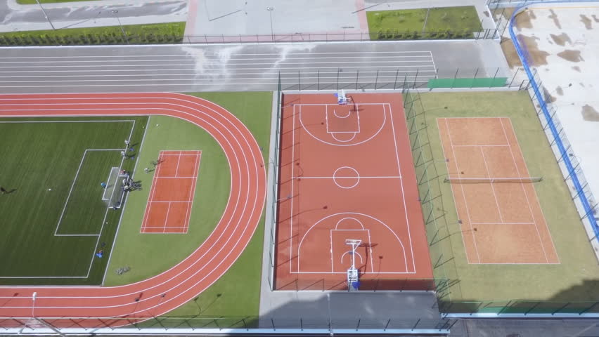 A complex of new sports facilities: a hockey field, a tennis court, a basketball court, running tracks and a football field in a new microdistrict. On football field are teenagers play football Royalty-Free Stock Footage #33963595