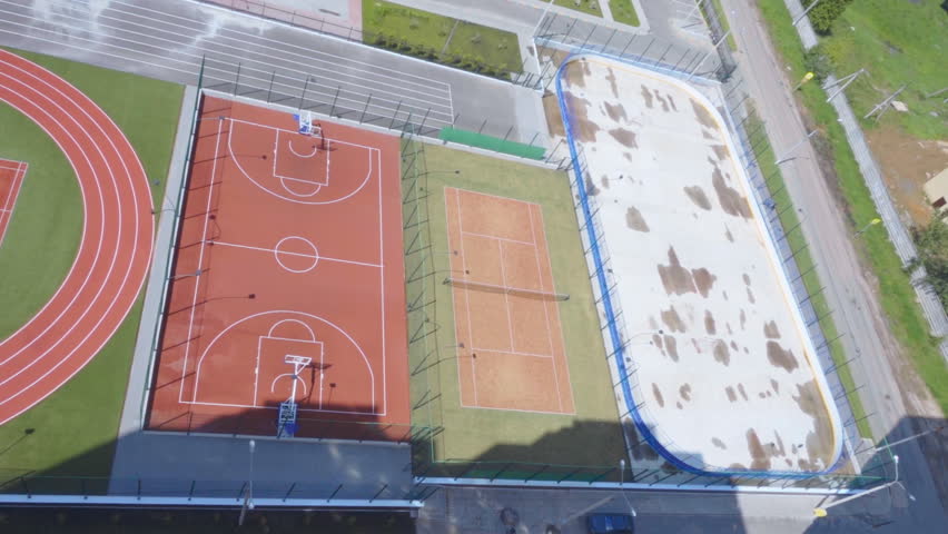 A complex of new sports facilities: a hockey field, a tennis court, a basketball court, running tracks and football field in new microdistrict. On football field are teenagers play football. Top view