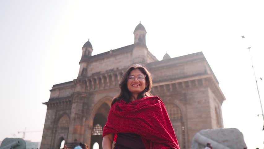 Portrait of beautiful smiling confident young Indian ethnic woman standing against Gateway of India at Mumbai, India. Pretty Indian woman face looking at camera posing outdoors.