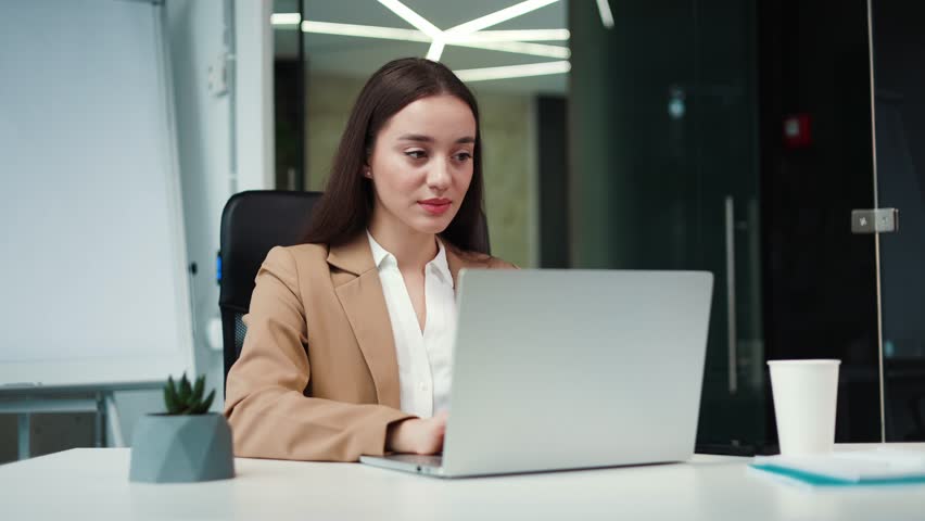 Portrait of pensive caucasian businesswoman sitting at desk in office and thinking while typing on portable laptop indoors. Beautiful female manager dreaming about coffee break in working time. Royalty-Free Stock Footage #3396414529