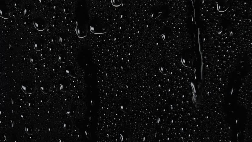 water drops flow down the surface of glass on black background. 