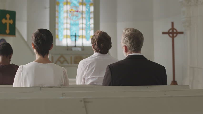 Back view slowmo of group of diverse parishioners sitting on benches in front of Black male pastor preaching sermon from tribune in Lutheran church Royalty-Free Stock Footage #3396431229