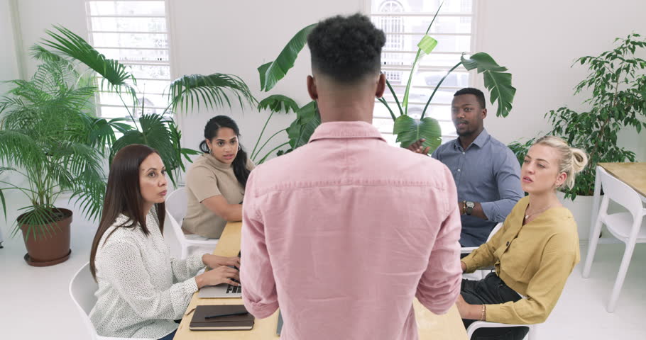 Creative businessman, coaching and presentation in meeting for staff training, agenda or tasks at office. Rear view of man or mentor talking to employees in team discussion for startup at workplace