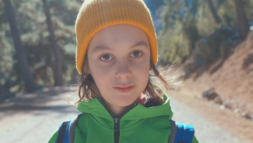 Portrait of a boy in a yellow hat with a backpack in the forest on a hike. A child stands in the middle of a road in the forest and looks at the camera. hiking and traveling.