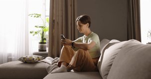 Happy smiling lady sits on sofa, savoring free time with modern technology, smiling contentedly. Peaceful moments, tranquility, happiness. Smartphone conversation with close people. Cinematic AD