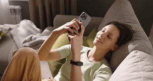 Attractive laughing girl reclined on sofa, savoring her free time, conversation with close people boyfriend using smartphone. Peaceful moments tranquility and happiness. Cinematic advertising.