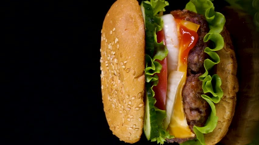 Delicious burger on the background of fire. Delicious burger with fresh iceberg cabbage, onions, tomatoes and grilled steak. Fast food, slow motion, Close-up, vertical footage
