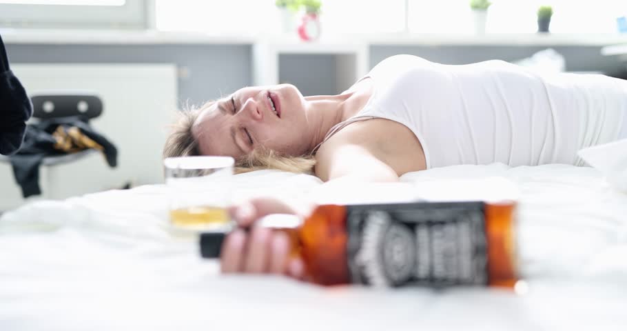 Drunk woman with a bottle of alcohol on the bed, close-up. Morning wake up after a party, hangover headache Royalty-Free Stock Footage #3396583703