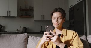 Modern woman using smartphone on sofa, chatting and browsing social media during her free time, searching information on browser wireless internet. Casual lifestyle and comfort. Cinematic advertising