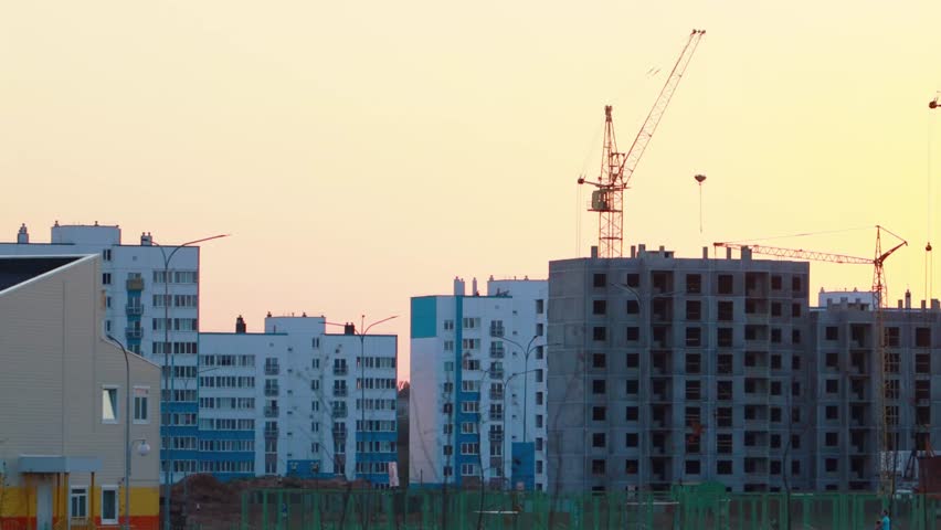 Construction of a new panel house in a microdistrict against the backdrop of sunset in the evening. Tall tower cranes against a sunset background. Copy space for text, immovables Royalty-Free Stock Footage #3396597343