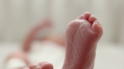 Newborn baby lying in cot. Baby is kicking and stretching legs. Closeup detail on soles of feet. Baby sweetly bends her big toe and touches her feet together.