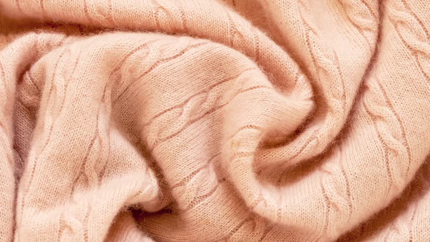 Video of textile background in beautiful pastel peach or trendy Peach Fuzz color. Soft, fluffy, warm mohair jumper with traditional braid pattern in soft pleats. Texture of clothes made of merino wool Royalty-Free Stock Footage #3396622729