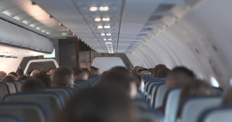 Back view, passengers sitting inside airplane cabin. Passenger flights, air travel. Calm, safe journey flight. People crowd traveling by commercial airlines. Interior of economy aircraft. Seat row