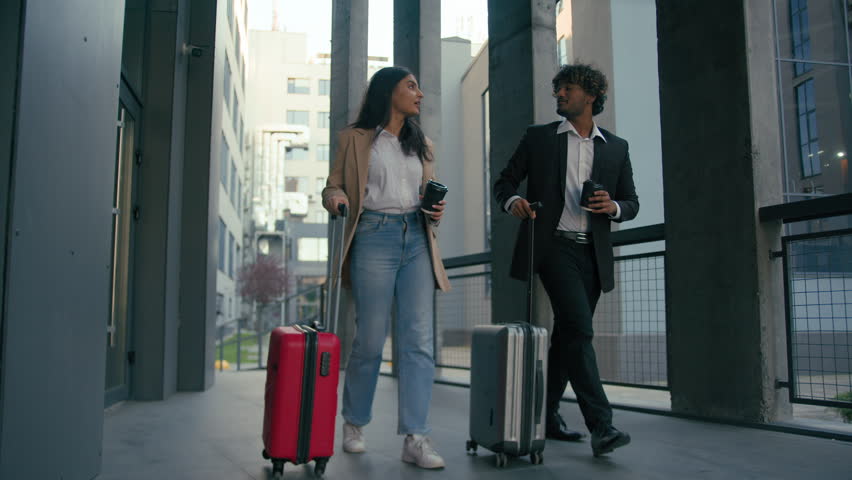 Indian Arabian business partners coworkers colleagues workers businessman and businesswoman passengers holding coffee cup talk walk with baggage luggage travel bags suitcases walking in city talking Royalty-Free Stock Footage #3396748531