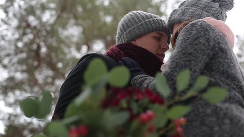 Newlyweds groom and bride hug kiss and warm each other in snowy pine forest during snowfall in slow motion. . Young couple in winter wood. Woman with bouquet. Valentine's Day and Video compilation.