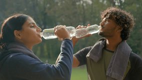 Indian Arabian couple drink after fitness workout outdoors healthy sport man and woman tired exhausted thirsty after exercise drinking water fitness bottle refresh wipe sweat with towel fit in park - Powered by Shutterstock - Get 15% off with code: PIKWIZARD15